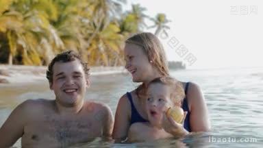 幸福的年轻父母和小儿子在海边放松，靠近海岸的棕榈树母亲和儿子吃苹果